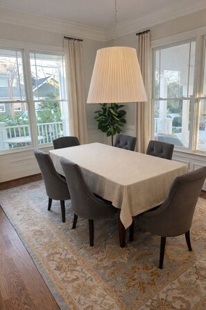 A dining room with a table set for six, surrounded by chairs, a hanging lamp, and a view of the outdoors through large windows. - Upscale 5BR House in Morningside – Perfect for World Cup Groups (Atlanta)