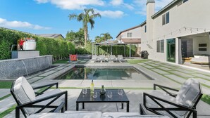 A modern outdoor pool area with lounge chairs and a table, surrounded by a well-maintained lawn and a house. - The Headliner:Private! Game Room! Festivals! (Coachella)