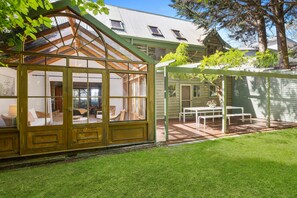 A conservatory with a glass roof, wooden beams, and a view of the garden.