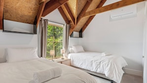 Une chambre avec deux lits, des poutres en bois, une fenêtre avec des rideaux et un appareil de climatisation.