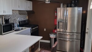 A compact kitchen with white cabinets, a stainless steel refrigerator, a microwave, and a coffee maker. - Spacious 2-bedroom house in enchanting Kansas City with AC, NSD-STRMAJ-00254  (Kansas City)
