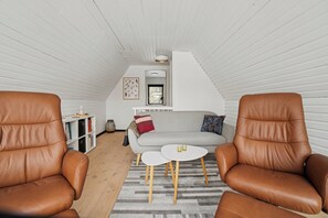 A cozy room with two leather chairs, a sofa, a small white table, and a bookshelf. - Holiday home near beach and Limfjord (Thyholm)