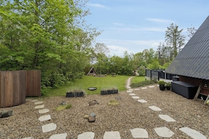 A gravel path with stepping stones leading to a wooden deck, surrounded by greenery and a small wooden structure. - Holiday home near beach and Limfjord (Thyholm)
