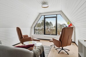 A room with a sloped ceiling, a large window, two brown chairs, a small round table, and a white desk. - Holiday home near beach and Limfjord (Thyholm)