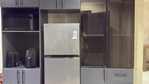 Een compacte keuken met inbouwapparatuur, waaronder een koelkast, magnetron en koffiezetapparaat, en een glazen kast.