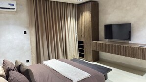 Een moderne slaapkamer met een groot bed, een flatscreen televisie bevestigd aan een houten paneel, en een ingebouwde bank.