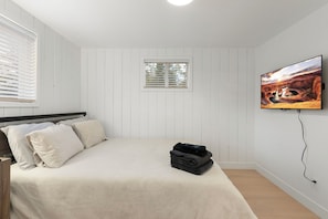 Une chambre à coucher avec un lit, des oreillers, une fenêtre et un téléviseur fixé au mur.