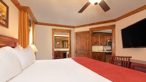 Camera d'albergo con un letto grande, una ventola a soffitto, mobili in legno, una televisione e vista sulla cucina.