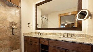 Un bagno con box doccia in vetro, un ampio specchio e uno specchio rotondo sopra, e mobili contenitori in legno.