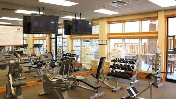 Una palestra con attrezzature per esercizi, ampie finestre e uno schermo televisivo.