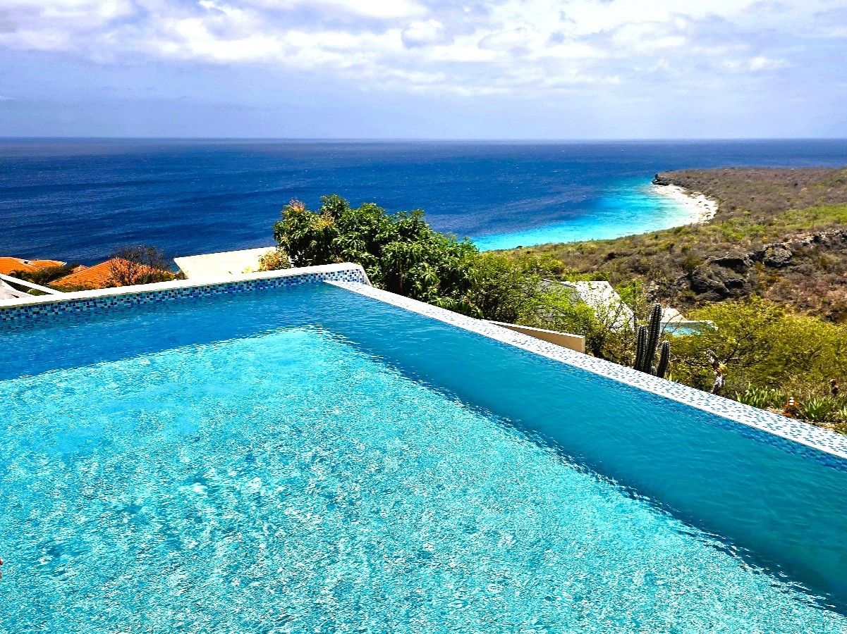 Una piscina con agua cristalina azul, rodeada de vegetación y con vistas a la costa.