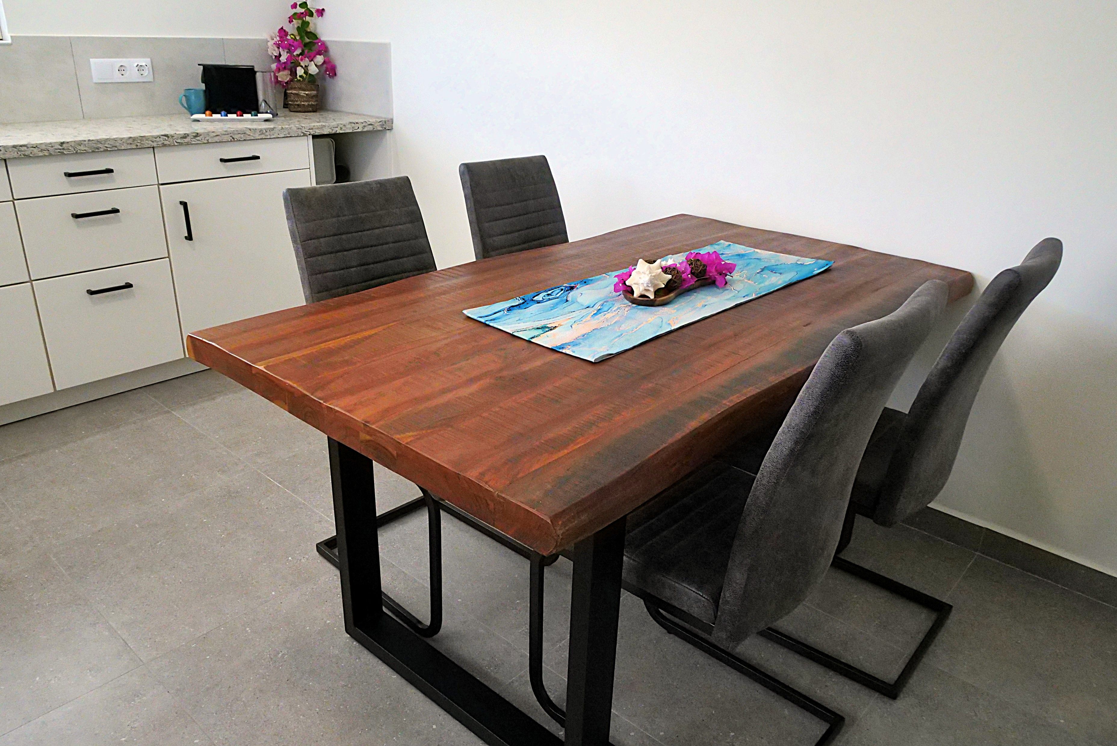 Een eettafel met stoelen, een vaas met bloemen en een schilderij op de tafel.