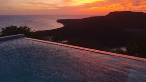 Vista del atardecer desde una zona junto a la piscina con vistas a una costa con acantilados.