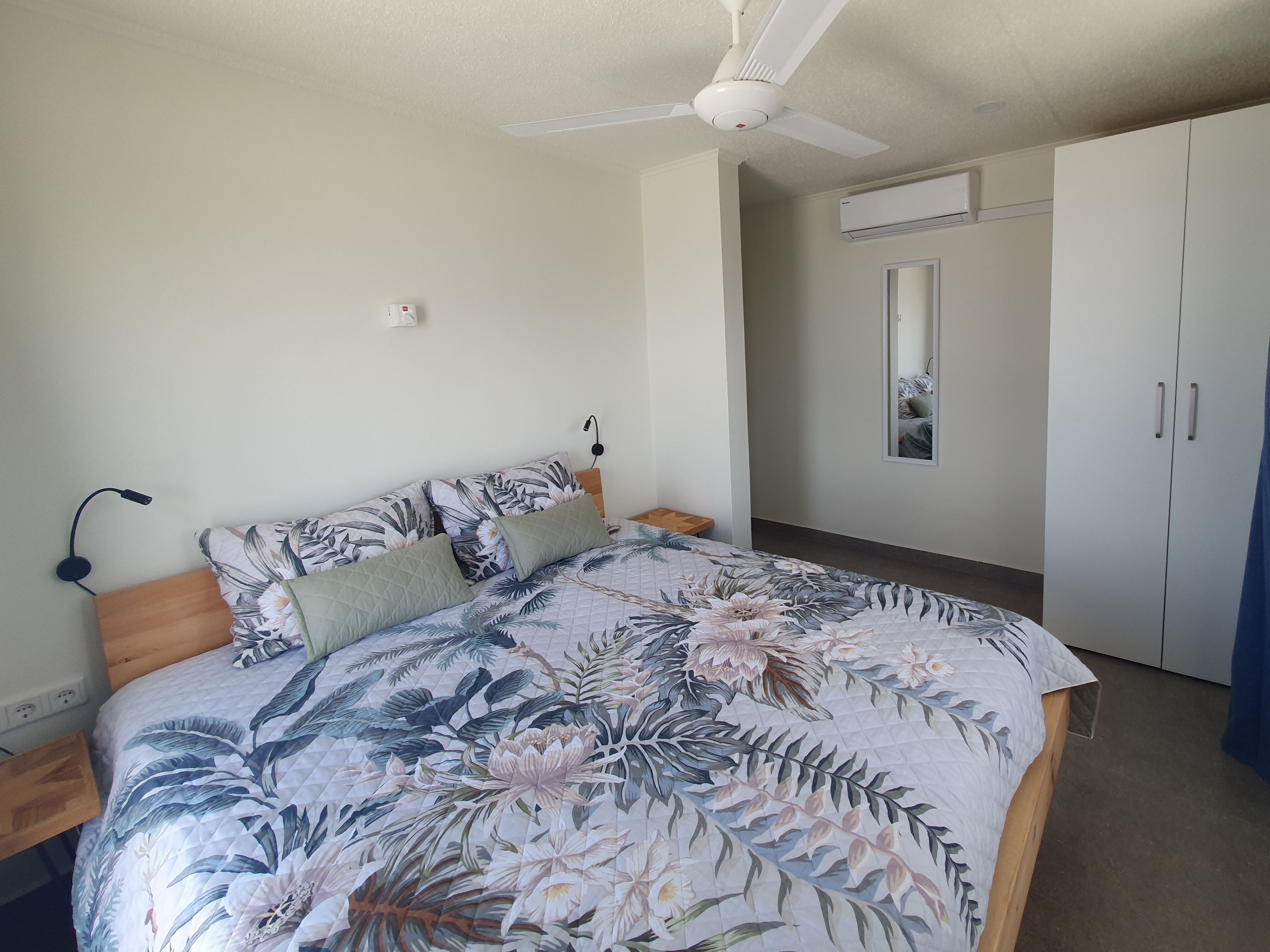 Een slaapkamer met een bed, een plafondventilator, een garderobe en een spiegel.