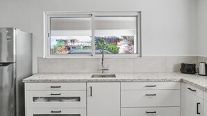 Cocina moderna con refrigerador empotrado, pileta de acero inoxidable y ventana con vista a un jardín y edificios.