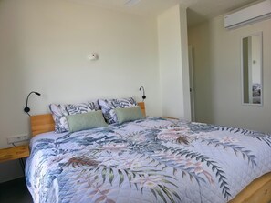 Et soveværelse med blomstret sengetæppe, træsenggavl, sengeborde med lamper og en vægmonteret aircondition.