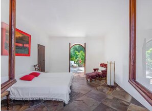 Ein Schlafzimmer mit Bett, Stuhl, Tisch und Blick ins Freie.