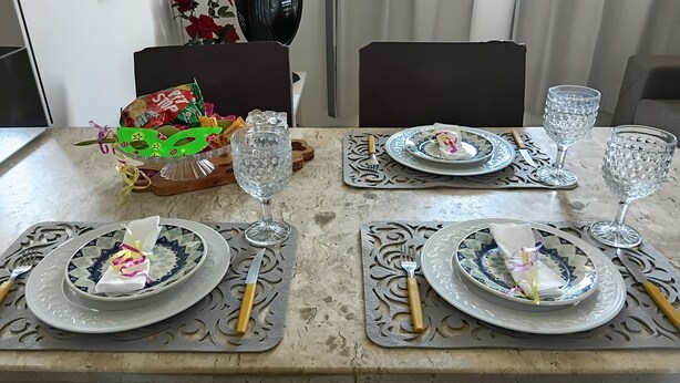 Une table à manger dressée avec des assiettes, des couverts et de la verrerie, agrémentée d’un panier décoratif et d’un éventail en arrière-plan.