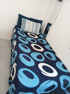Een klein, netjes opgemaakt bed met een donkerblauwe en witte bedspread en passende kussens.