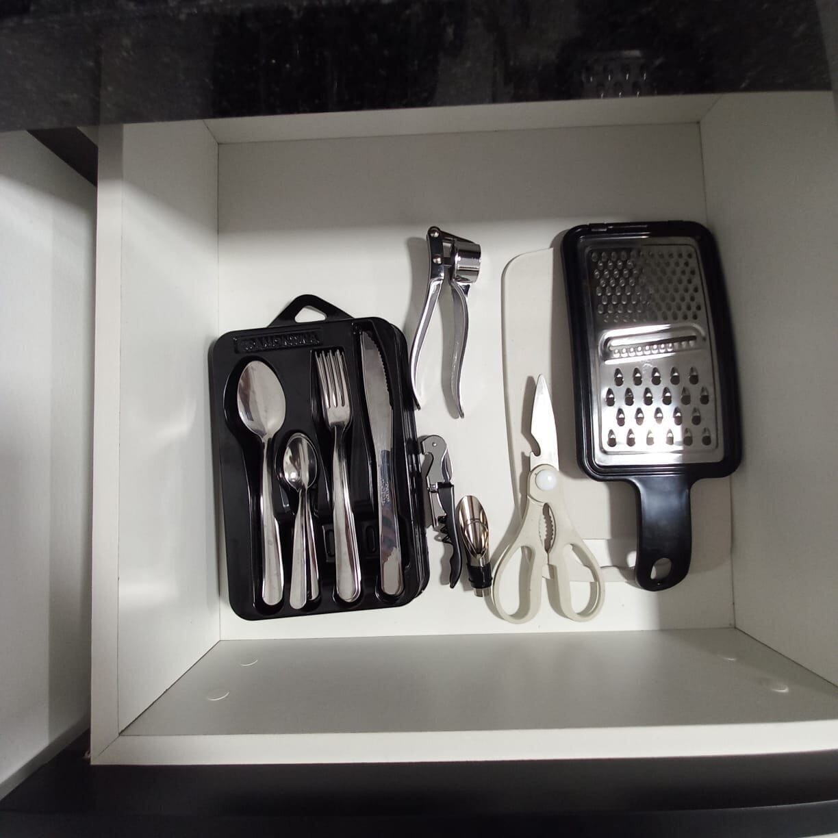 A kitchen drawer with a set of utensils including a grater, spoons, forks, and knives.