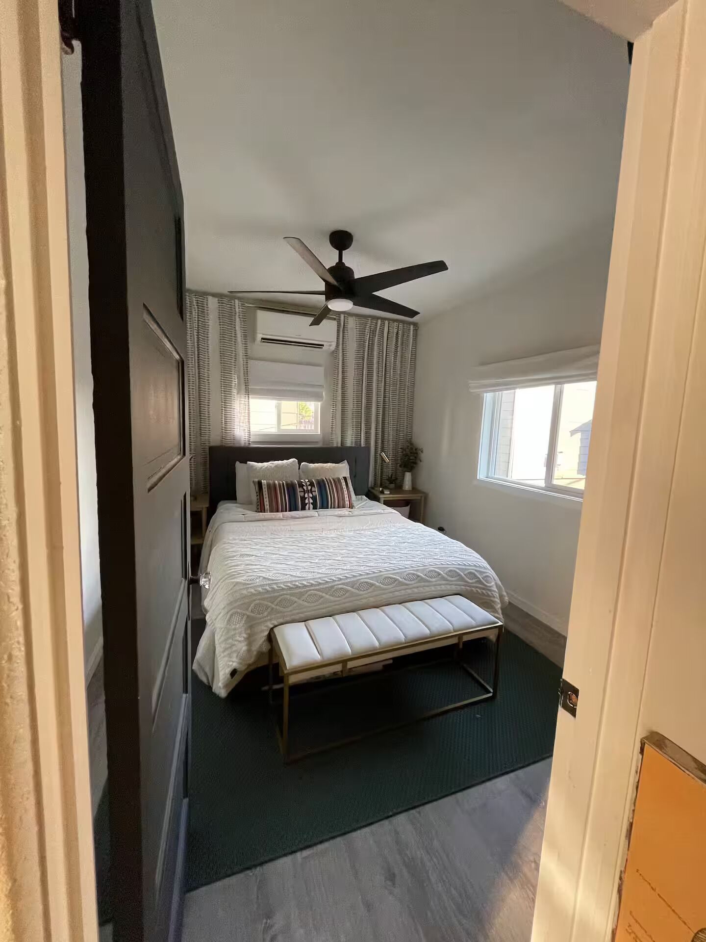Een slaapkamer met een bed, een bankje, een plafondventilator en een raam.