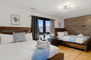 A hotel room with two beds, a window with curtains, a nightstand with a lamp, and a wooden wall panel. - Spa-Style Luxury Lodge w/ Sauna, Hot Tub & Games (Tannersville)