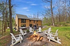 A lodge with a fire pit surrounded by Adirondack chairs, a deck, and a large wooden building. - Sleeps 24! Luxury, Sauna, Hot tub, Zen room, Gameroom, pets (Tannersville)