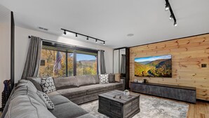 A modern living room with a sectional sofa, a coffee table, and a large TV on a wooden wall. - Sleeps 24! Luxury, Sauna, Hot tub, Zen room, Gameroom, pets (Tannersville)