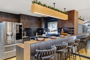 A modern kitchen with a stainless steel refrigerator, a built-in oven, and a large island with bar stools. - Spa-Style Luxury Lodge w/ Sauna, Hot Tub & Games (Tannersville)