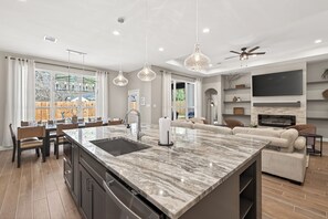 Une cuisine moderne dotée d’un grand îlot central, d’un coin repas et d’un salon avec une cheminée.