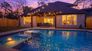 Una piscina residenziale con luci a stringa, un patio coperto con sedie e vista sulla casa.