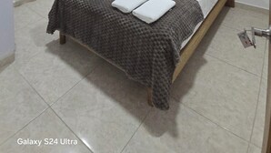 A bedroom with a bed, pillows, a bedside table, a window with curtains, a shelf with decorative items, and a door. - Casa Sandunguera (Cartagena)
