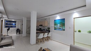 A modern living room with a Galaxy S24 Ultra TV, a dining area with white chairs, a kitchen with marble countertops, and a painting on the wall. - Casa Sandunguera (Cartagena)