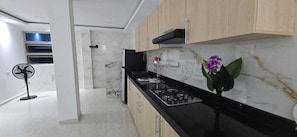 A modern kitchen with marble countertops, a gas stove, and wooden cabinets. - Casa Sandunguera (Cartagena)