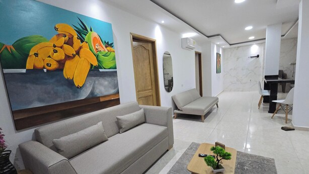 A modern hotel lobby with a grey sofa, a coffee table with a bonsai, a painting of bananas, and a marble wall. - Casa Sandunguera (Cartagena)