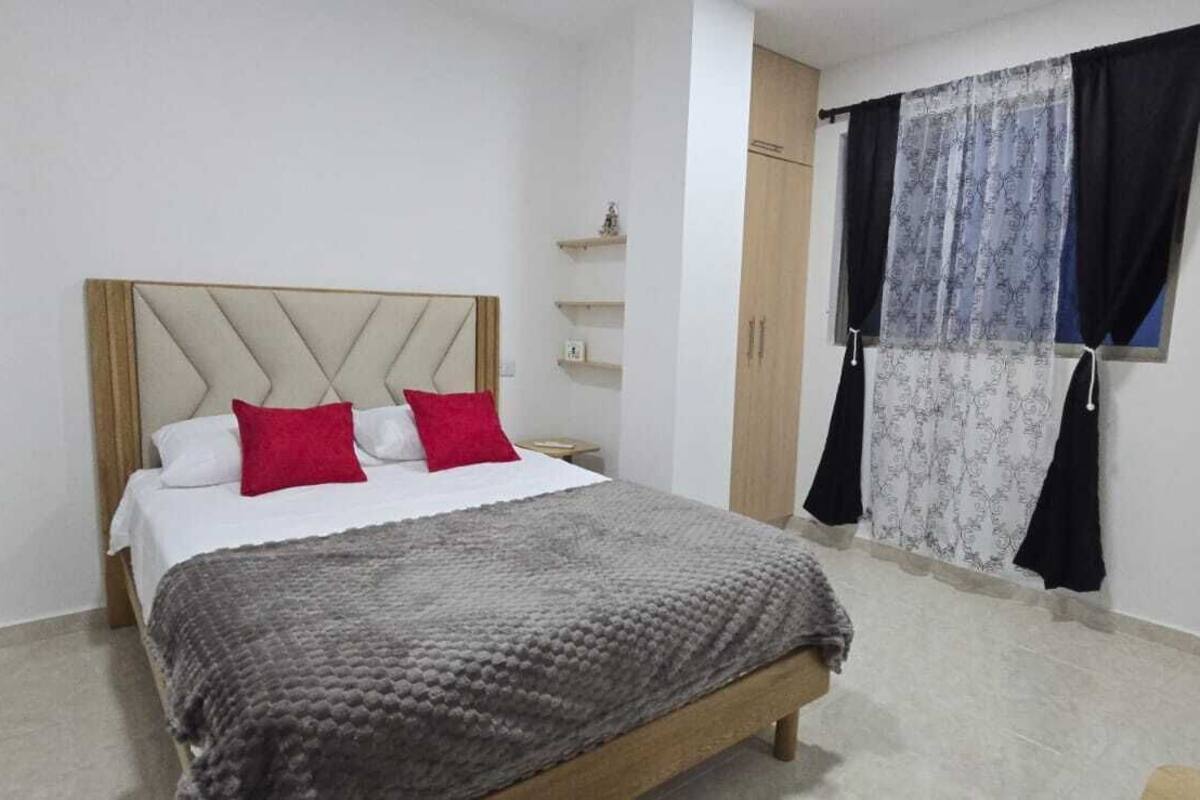A bedroom with a bed, a headboard, a window with curtains, and a bedside table.