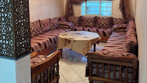 A room with a large, ornate sofa set, a wooden coffee table, and a chandelier. - Premium Apartment | 5 Min from Rabat-Salé Airport | Free Parking & WiFi (Sale)