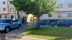 A paved pathway with parked cars, a tree, and a building with multiple windows and balconies. - Premium Apartment | 5 Min from Rabat-Salé Airport | Free Parking & WiFi (Sale)