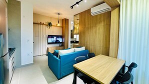 A modern living room with a blue sofa, a wooden dining table, and a TV mounted on the wall. - Studio New Home | Practicality in one place. (Uberlândia)