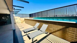A rooftop pool area with two sun loungers, a pool, and a tiled wall. - Studio New Home | Practicality in one place. (Uberlândia)