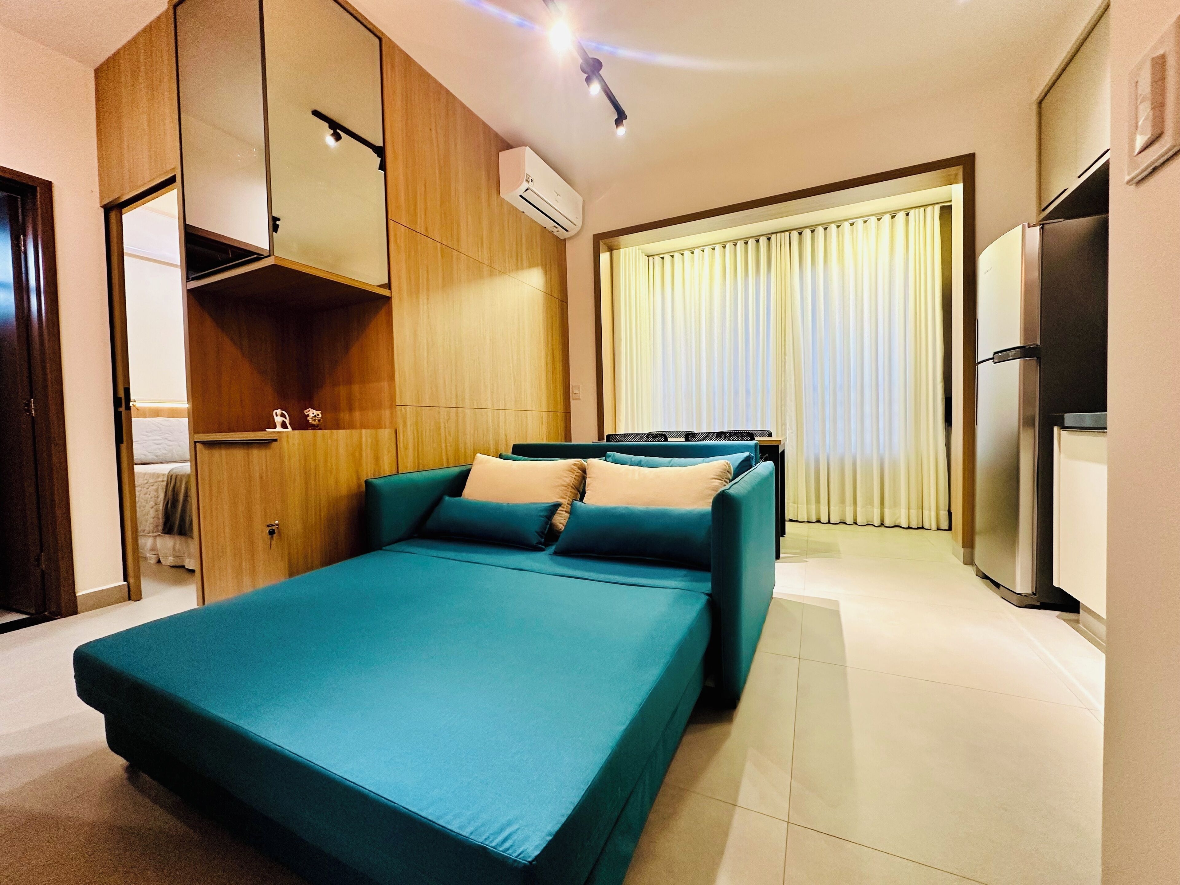 A modern bedroom with a teal bed, wooden wardrobe, and a built-in air conditioning unit.