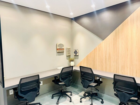 Une salle de réunion moderne, dotée d’une table en verre, de quatre chaises de bureau noires et d’une décoration murale tissée.