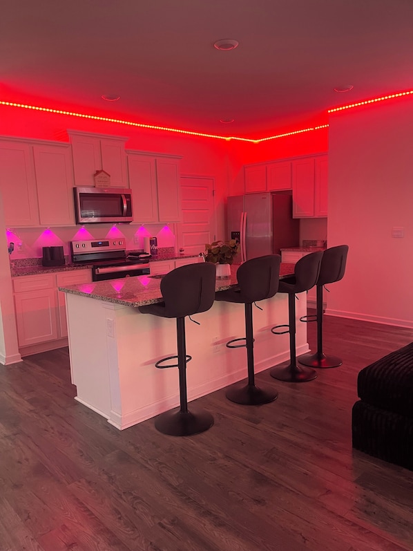 A modern kitchen with white cabinets, a central island with bar stools, and red ambient lighting.