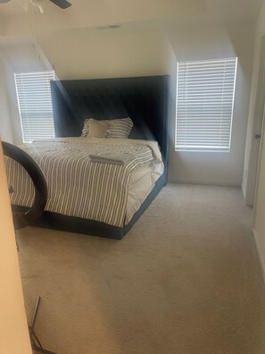 A bedroom with a bed, a ceiling fan, and two windows with blinds.