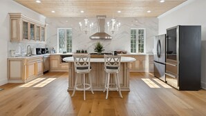 Une cuisine moderne avec des meubles en bois, un pare-feu en marbre, un îlot central doté de tabourets et un grand réfrigérateur.