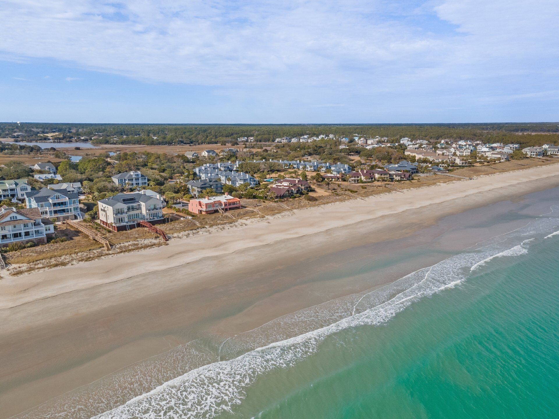 Una zona residencial costera con casas a lo largo de la playa, cielo despejado y vista al océano.