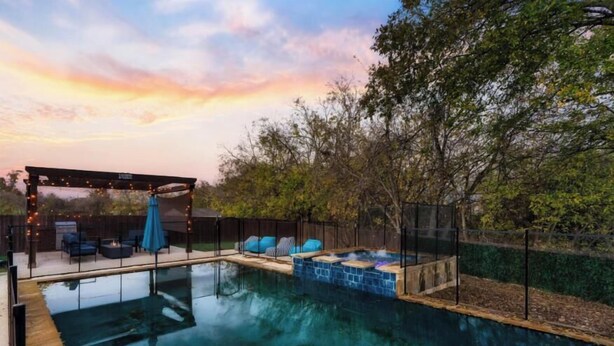 A backyard with a swimming pool, a hot tub, and a covered seating area with string lights. - Luxury 7BR Pool, Hot Tub & 4 Car Parking (Pflugerville)