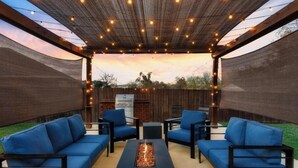 An outdoor patio with a fire pit, blue sofas, and string lights. - Luxury 7BR Pool, Hot Tub & 4 Car Parking (Pflugerville)