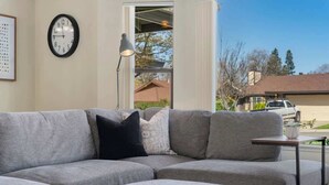 A modern living room with a sectional sofa, a side table, a floor lamp, and a wall clock. - Spacious 3BR/2BA Central Sac – Fireside Comfort (Sacramento)