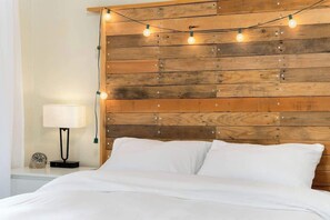 A bed with white bedding, a wooden headboard with string lights, a bedside lamp, and a clock on the nightstand.